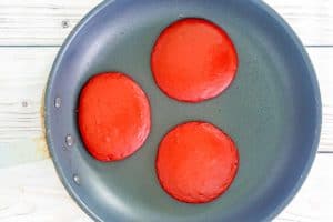 three red velvet pancakes cooking in a skillet.