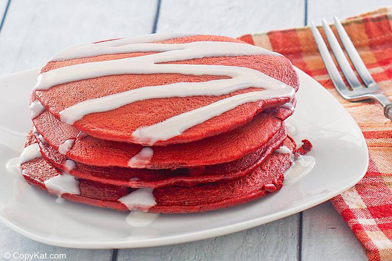 four red velvet pancakes with cream cheese glaze on a plate.