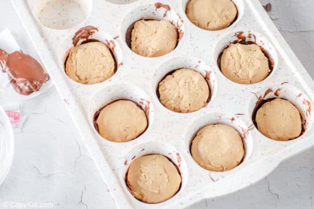 peanut butter patties on top of chocolate in a muffin pan.