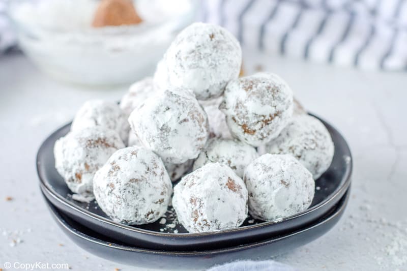 powdered sugar coated rum balls stacked on a black plate.