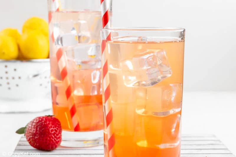 two glasses of homemade Sonic strawberry lemonade, a strawberry, and lemons.