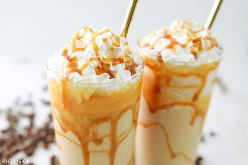 two homemade Starbucks caramel frappuccino drinks topped with whipped cream and caramel sauce.