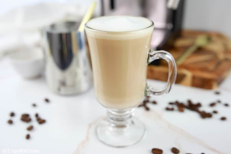 homemade Starbucks flat white coffee, coffee beans, frothing cup, and espresso machine.