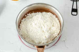 adding flour, sugar, and cocoa powder to a chocolate mixture in a saucepan.
