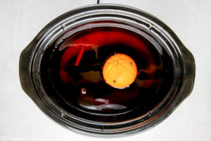 wassail mixture and an orange studded with cloves in a crockpot slow cooker.