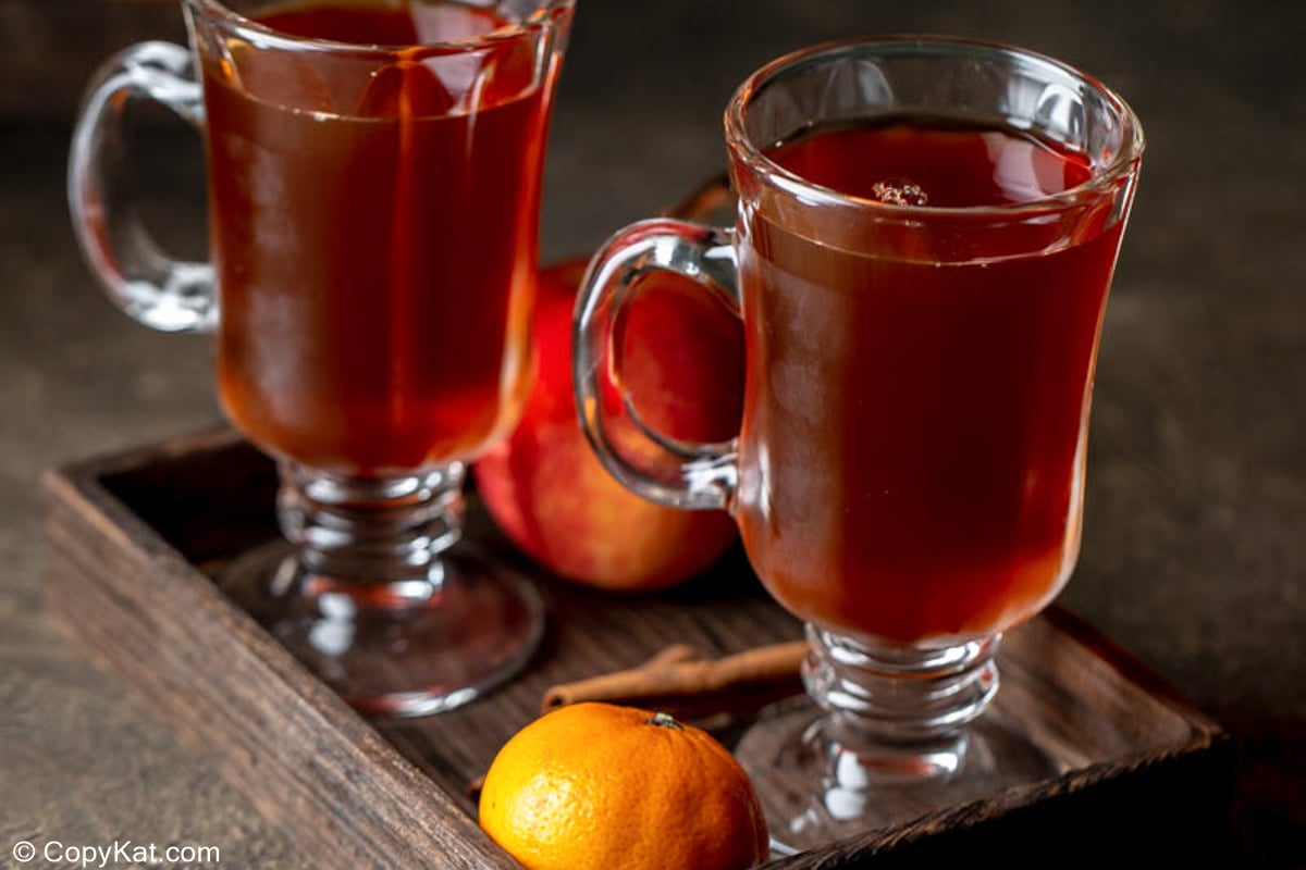 wassail in two glass mugs, an orange, and apple.