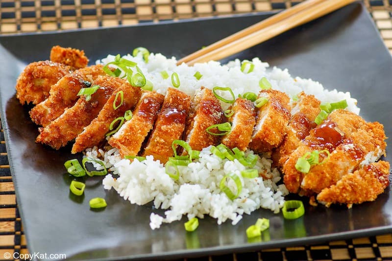 slices of chicken katsu and white rice on a black plate.