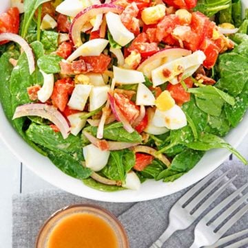 overhead view of spinach salad and a bowl of hot bacon dressing.