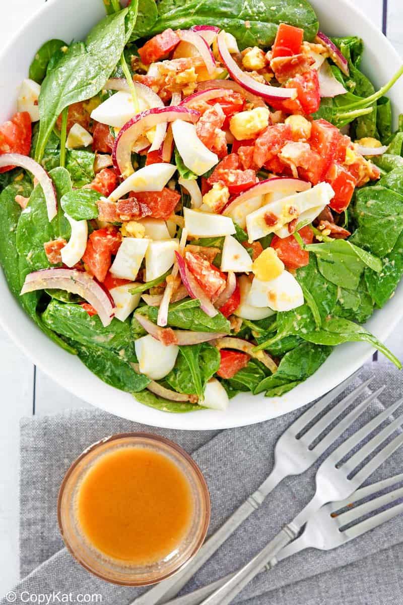 overhead view of spinach salad and a bowl of hot bacon dressing.