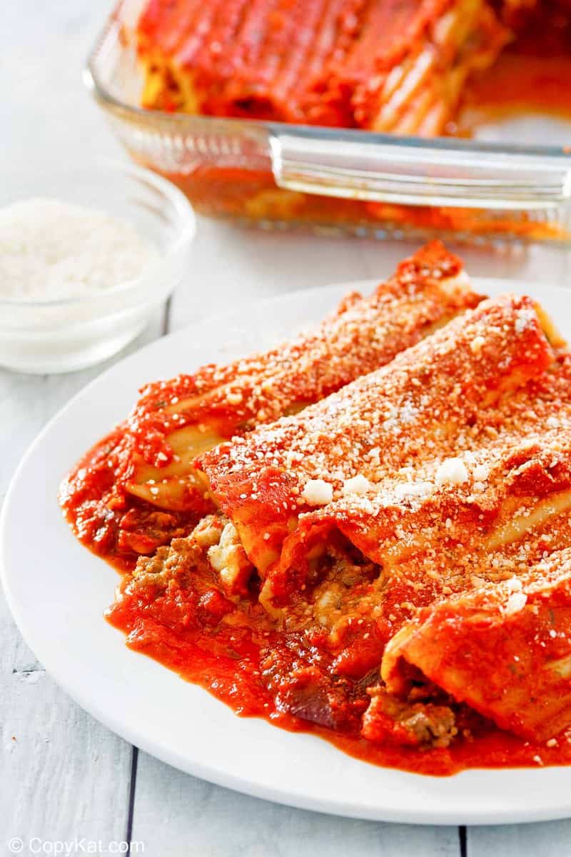 meat and cheese stuffed manicotti on a plate and a bowl of grated romano cheese.
