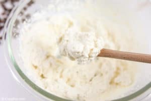 vanilla whipped cream on a wood spoon over a bowl of it.