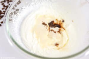 sugar and vanilla extract added to whipped cream in a bowl.