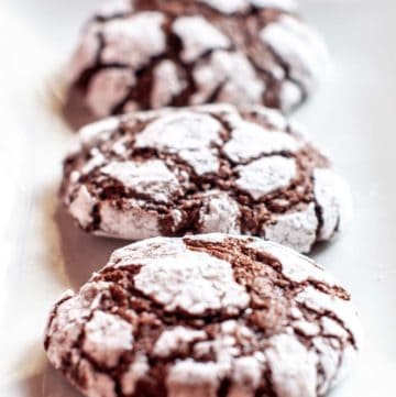 three chocolate crinkle cookies on a plate.