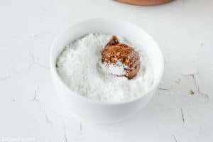 chocolate crinkle cookie dough ball in a bowl of powdered sugar.