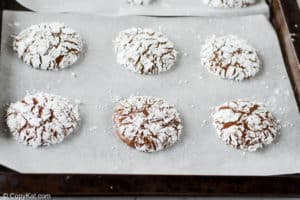 six chocolate crinkle cookies on a baking sheet.