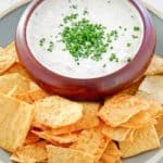 a bowl of clam dip and crackers on a platter.