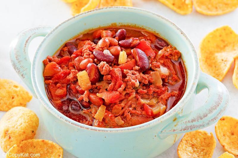 a bowl of crockpot chili and corn chips scattered around it.