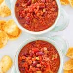 overhead view of two bowls of crockpot chili and corn chips.