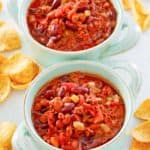 crockpot chili in two bowls and corn chips scattered around them.