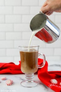 pouring steamed milk into a mug with peppermint chocolate syrup and coffee.