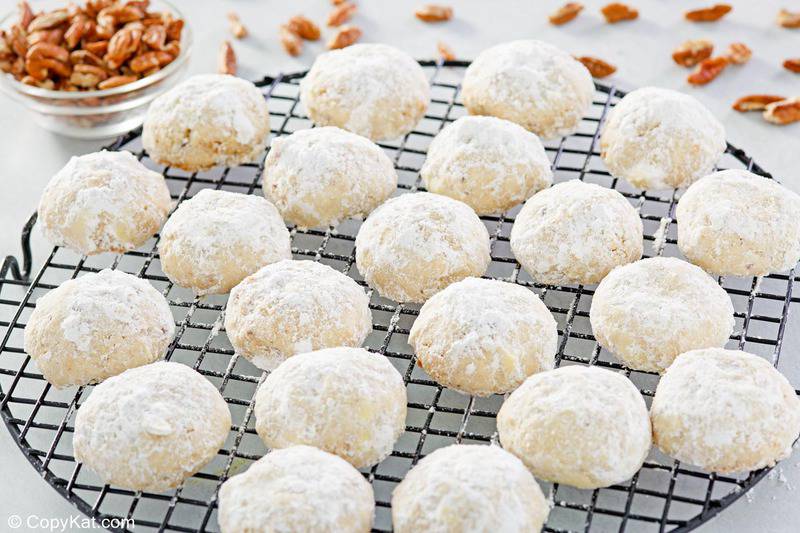 pecan sandies cookies on a wire rack and a bowl of pecans.