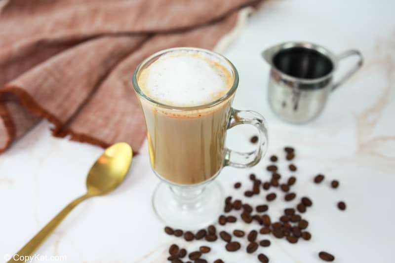 homemade Starbucks smoked butterscotch latte, coffee beans, spoon, and small metal pitcher.