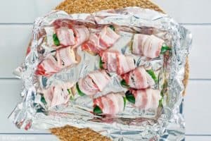 bacon wrapped jalapeno poppers on a baking sheet before cooking.