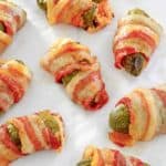 bacon wrapped jalapeno poppers scattered on parchment paper.