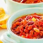Crockpot chili in two bowls and corn chips next to them.