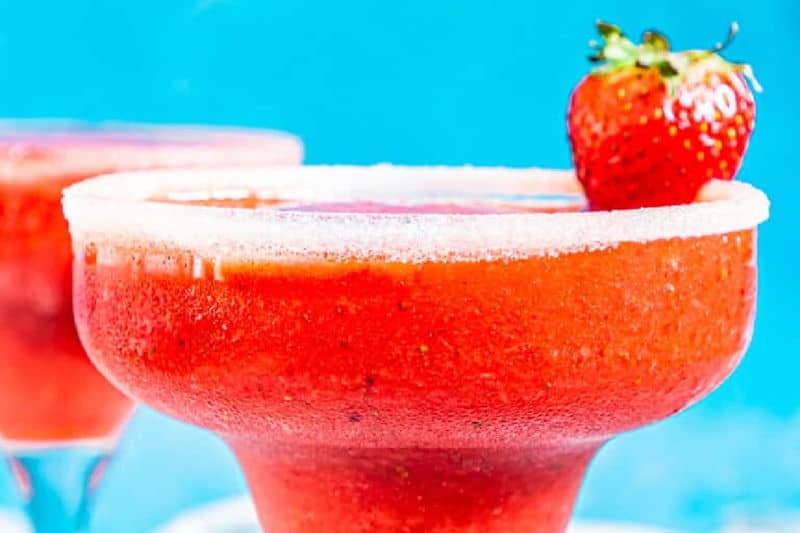 a glass filled with a strawberry daiquiri and a fresh strawberry