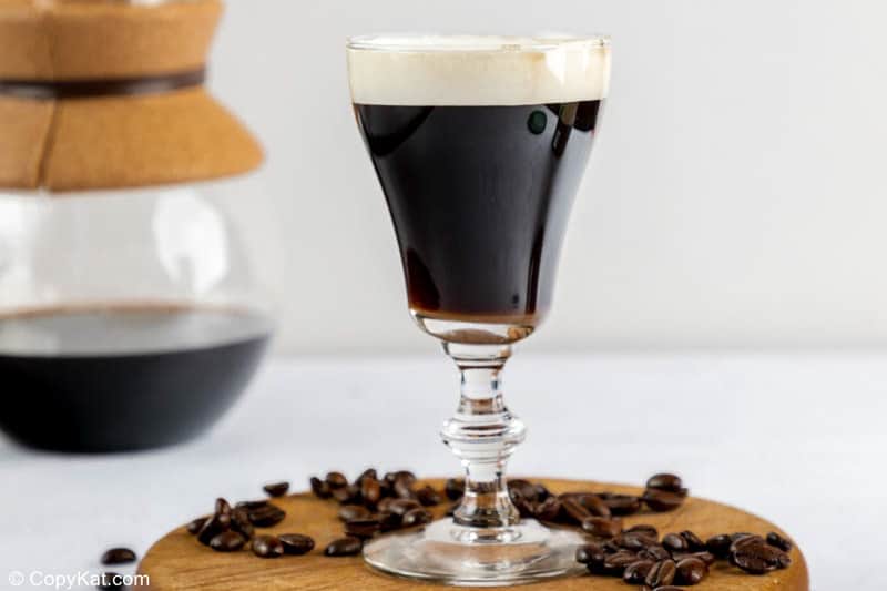 A classic Irish coffee drink with coffee beans scattered around it.