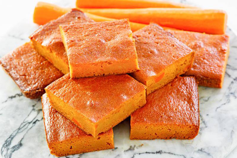stack of carrot pudding slices and three carrots behind it.