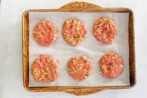 ground chicken patties on a parchment paper lined baking sheet.