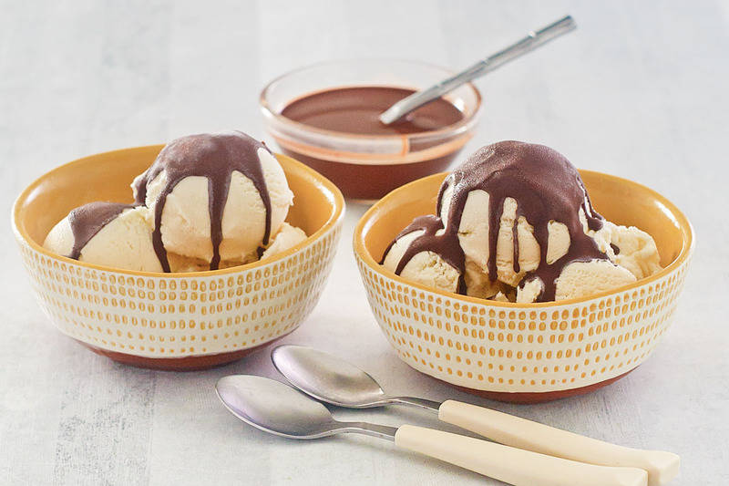 vanilla ice cream topped with homemade chocolate magic shell and two spoons.