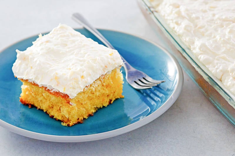 slice of mandarin orange cake and a fork on a plate next to the cake.