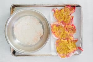 breading in a bowl and pork chops with mustard spread on them.