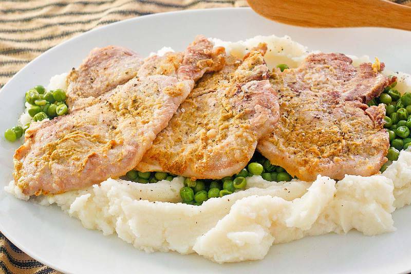 mustard pork chops on top of peas and mashed potatoes on a platter.
