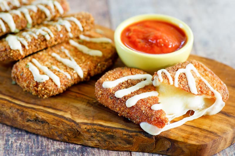 homemade Olive Garden fried mozzarella sticks with marinara sauce on a wood board.