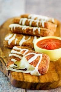 homemade Olive Garden fried mozzarella sticks and a cup of marinara sauce on a wood board.