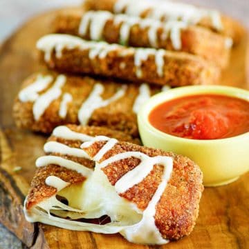 homemade Olive Garden fried mozzarella sticks and a cup of marinara sauce on a wood board.