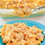 sausage mac and cheese casserole on spoon over a plate of it.
