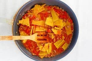 adding broken lasagna noodles to a skillet with meat sauce.