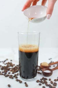 pouring caramel syrup into a glass with espresso.