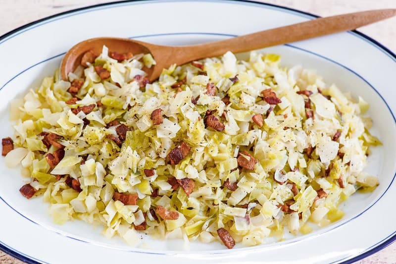 boiled cabbage with bacon on a white serving platter.