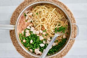 adding chicken, spaghetti, and peas to a pot.