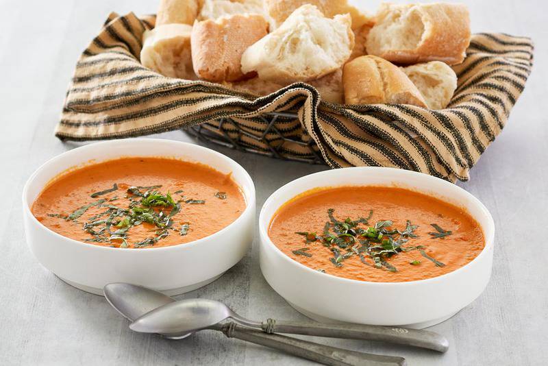 two bowls of copycat La Madeleine creamy tomato basil soup and a basket of bread.