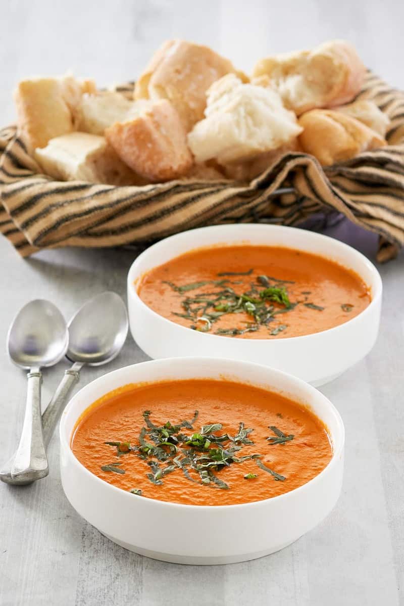 a basket of bread and two bowls of tomato basil soup.