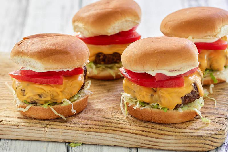 air fryer hamburgers with cheese and toppings on a wood board.