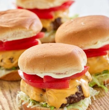 four air fryer hamburgers with cheese on a wood board.