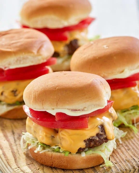 four air fryer hamburgers with cheese on a wood board.